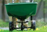 Person pushing a green lawn spreader