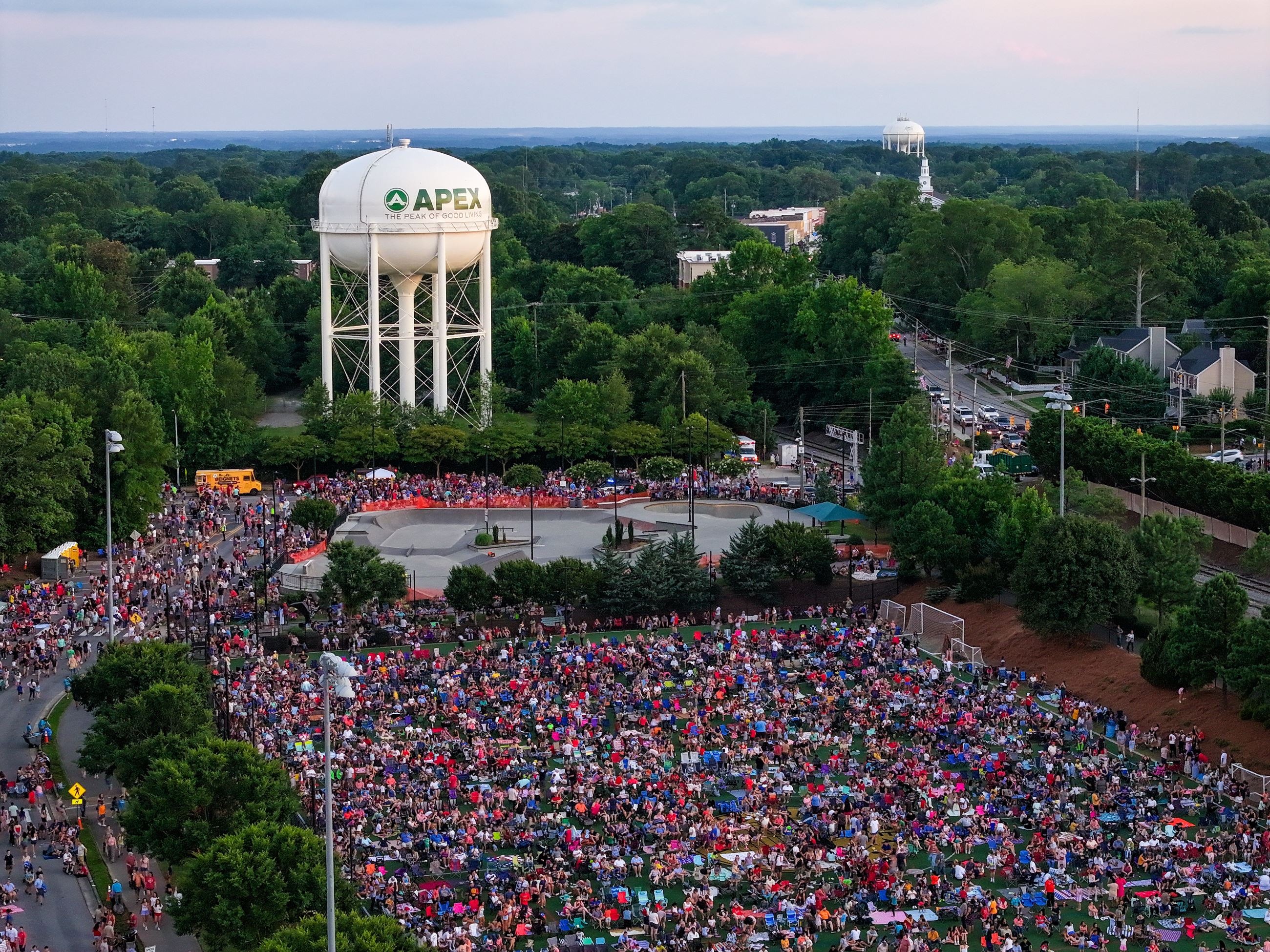 Aerial view of a large outdoor gathering at dusk, with a massive crowd seated on a grassy field.